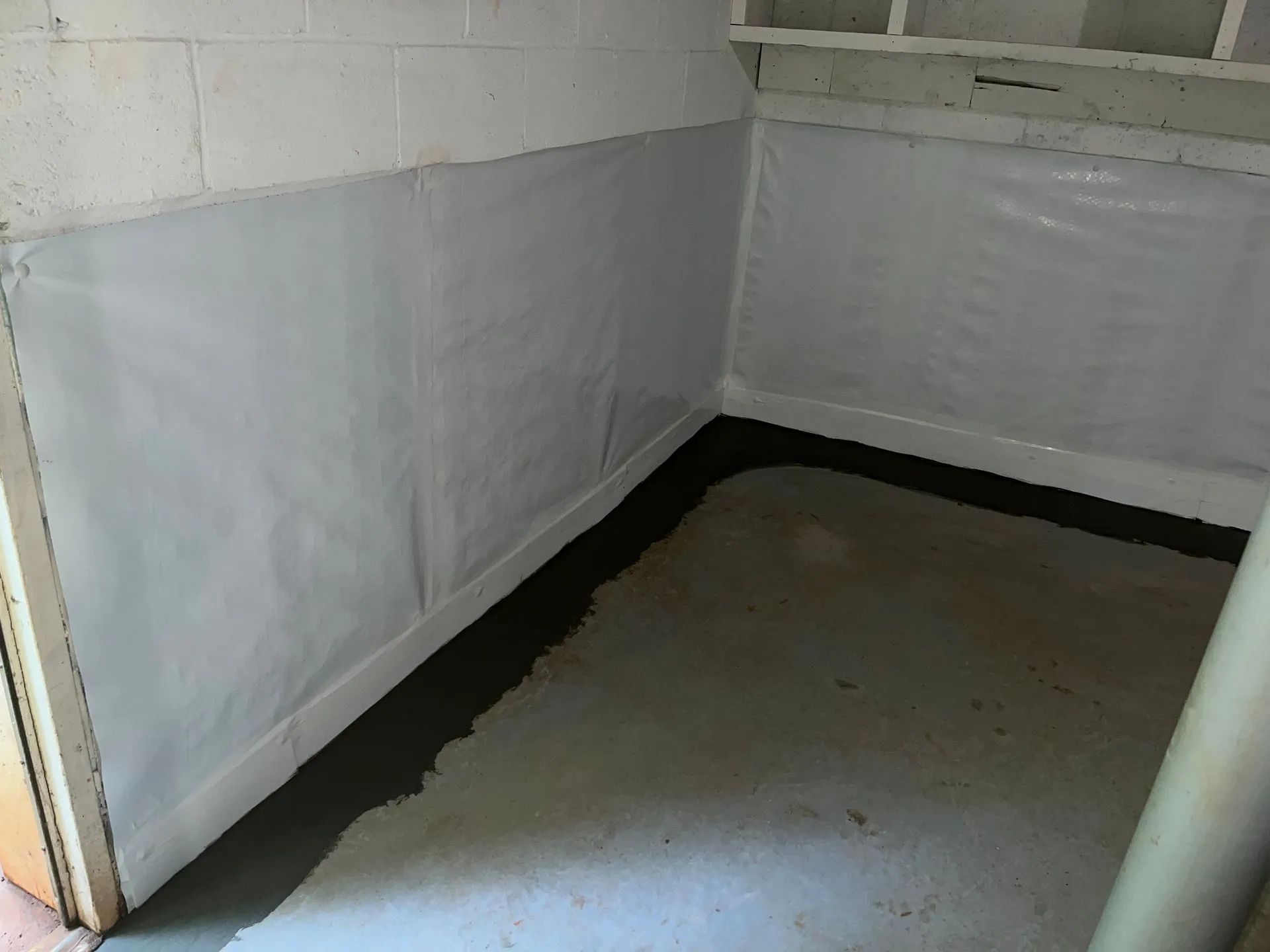 Empty white basement corner with gray floor and black waterproofing along the walls
