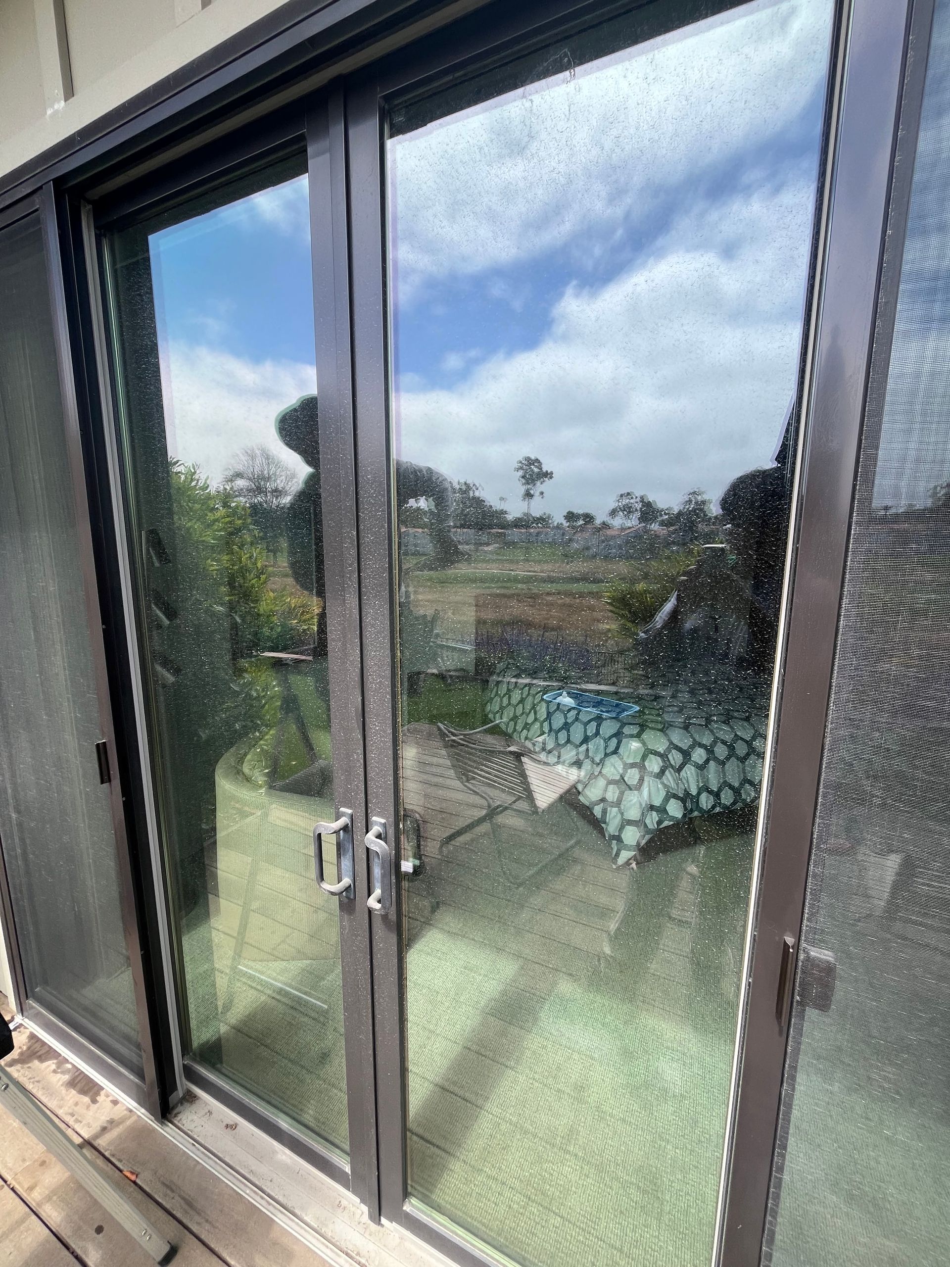 A view through a sliding glass door showing a bright backyard with a small pool, lawn, and sky reflected in the pane.