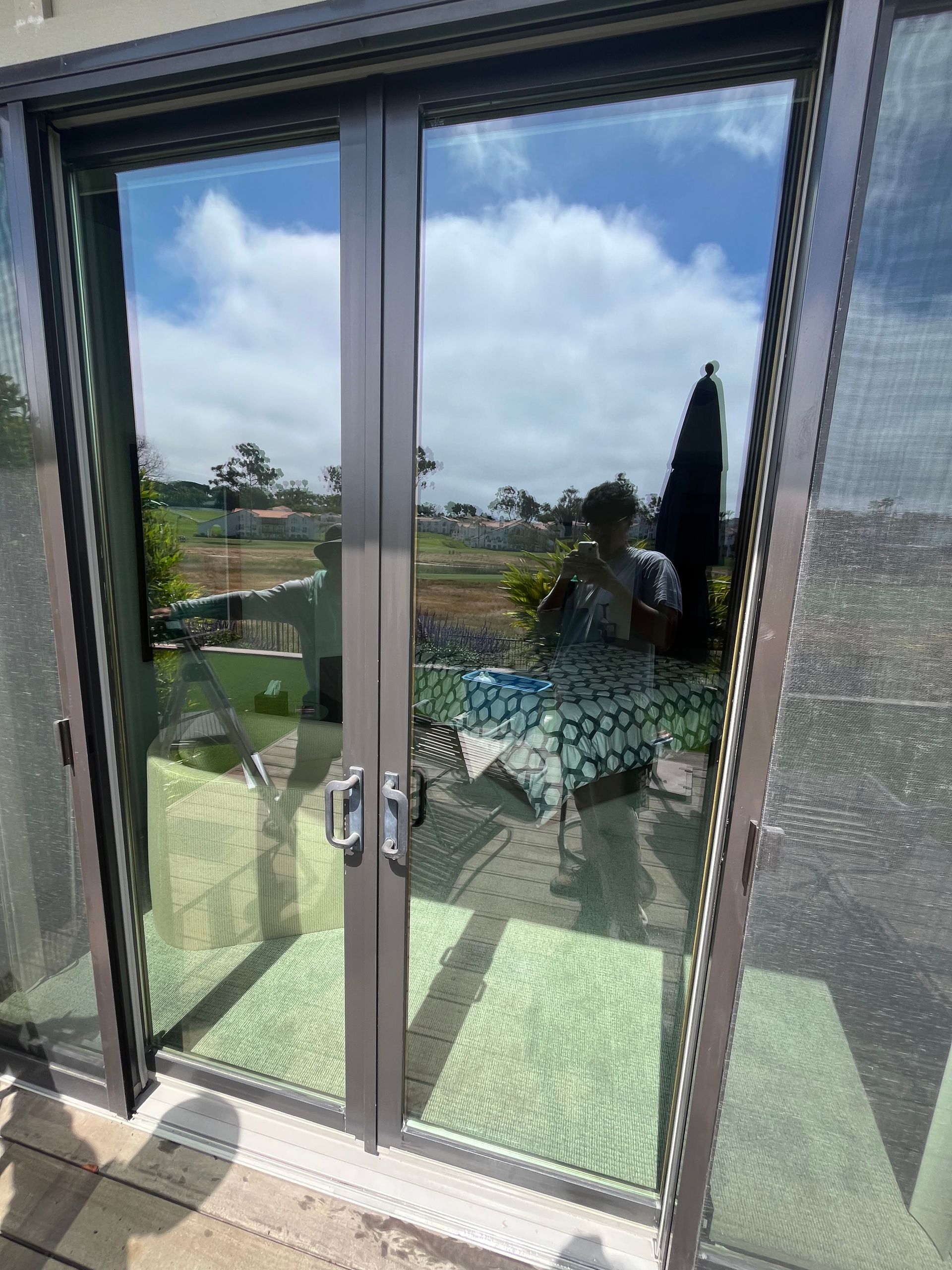 A reflection of a patio scene with a person, table, and umbrella seen in the glass panes of a set of sliding doors.