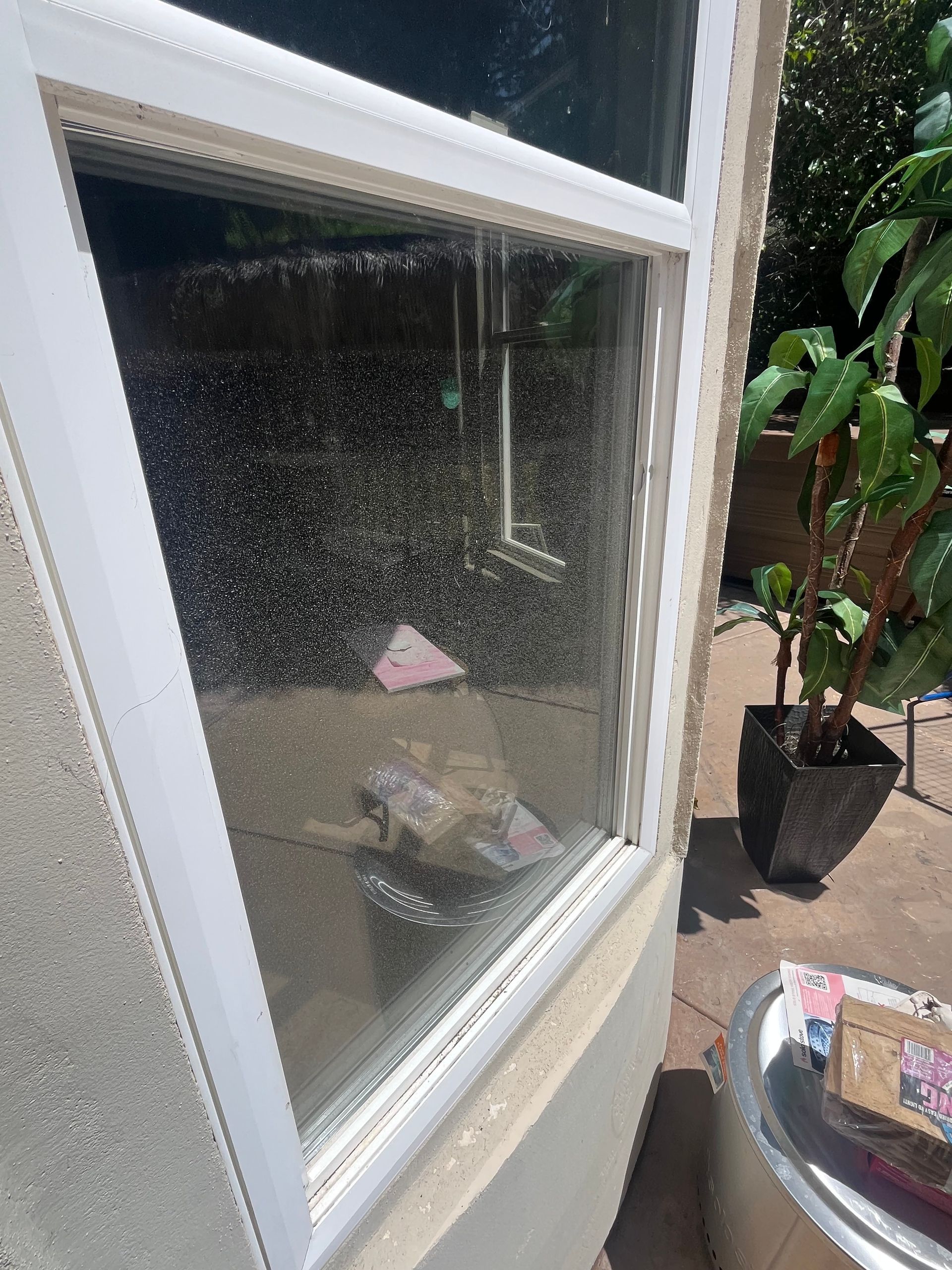 A white-framed window with a screen covered in small, dark spots, viewed from an outdoor patio.