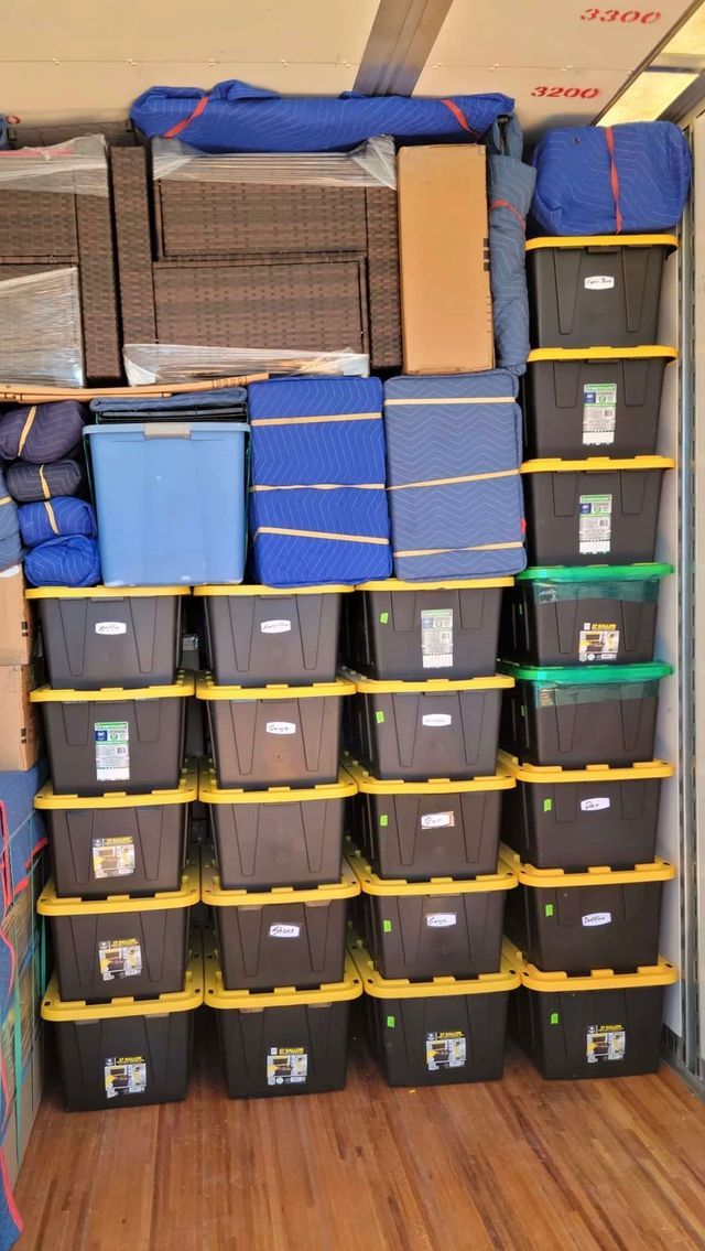 Stacked plastic storage bins and blue bags organized on shelves in a room with a wooden floor.