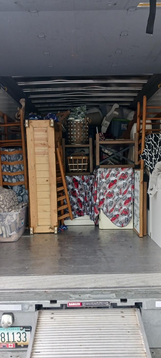 Open storage garage with shelves, stacked boxes, and rolled rugs inside a vehicle or trailer.