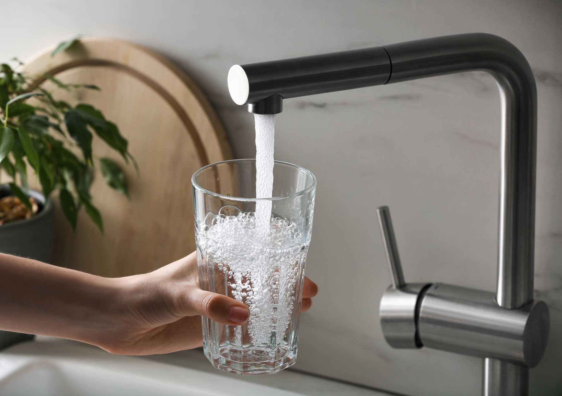 A person is pouring water into a glass from a faucet.