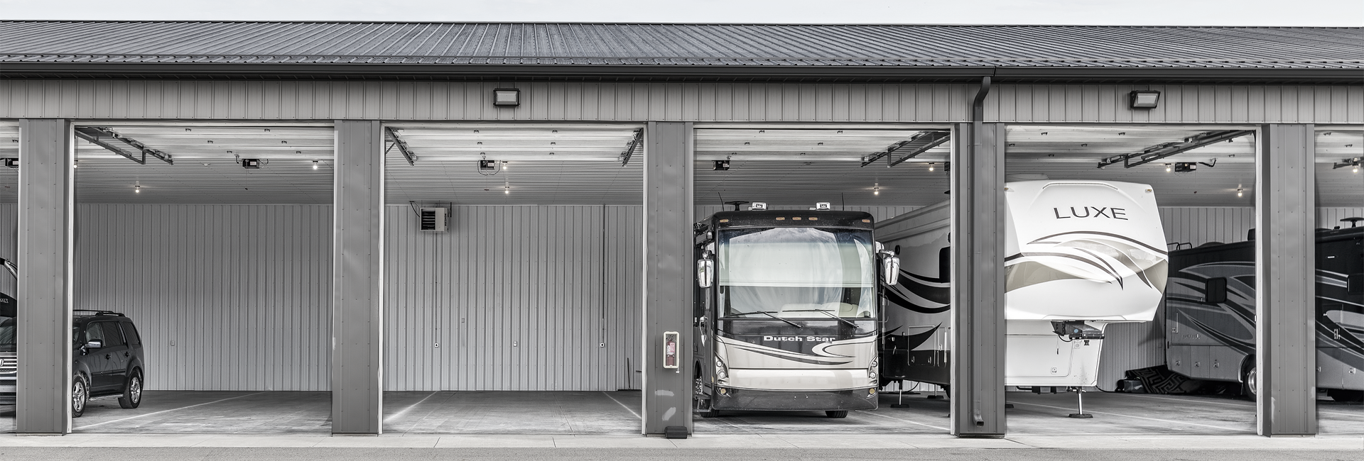 RV storage units, each with a vehicle inside. Gray metal structure. Daytime, overcast sky.