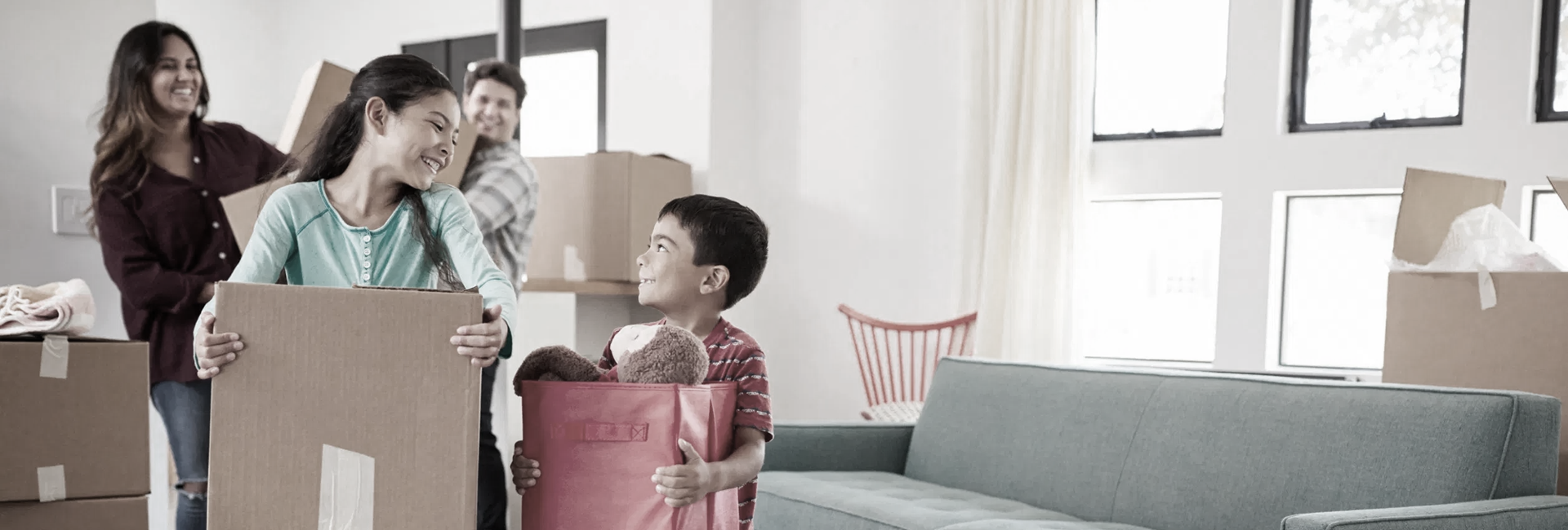 Family carrying boxes into a new home, smiling.