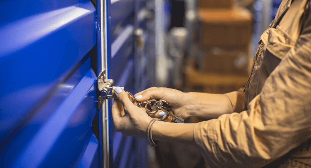 Person's hands opening a blue door with a lock. They are wearing an orange jumpsuit in a warehouse.