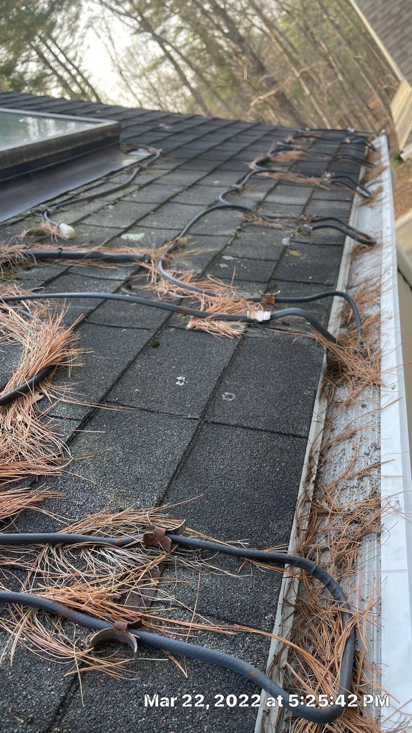 A roof with a gutter filled with leaves and wires.