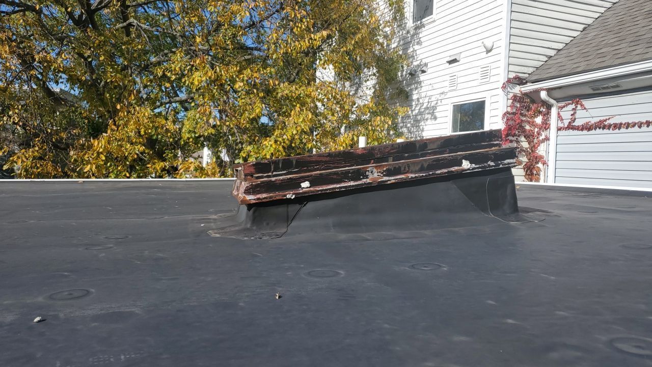 A roof with a drain hole in it and a tree in the background.