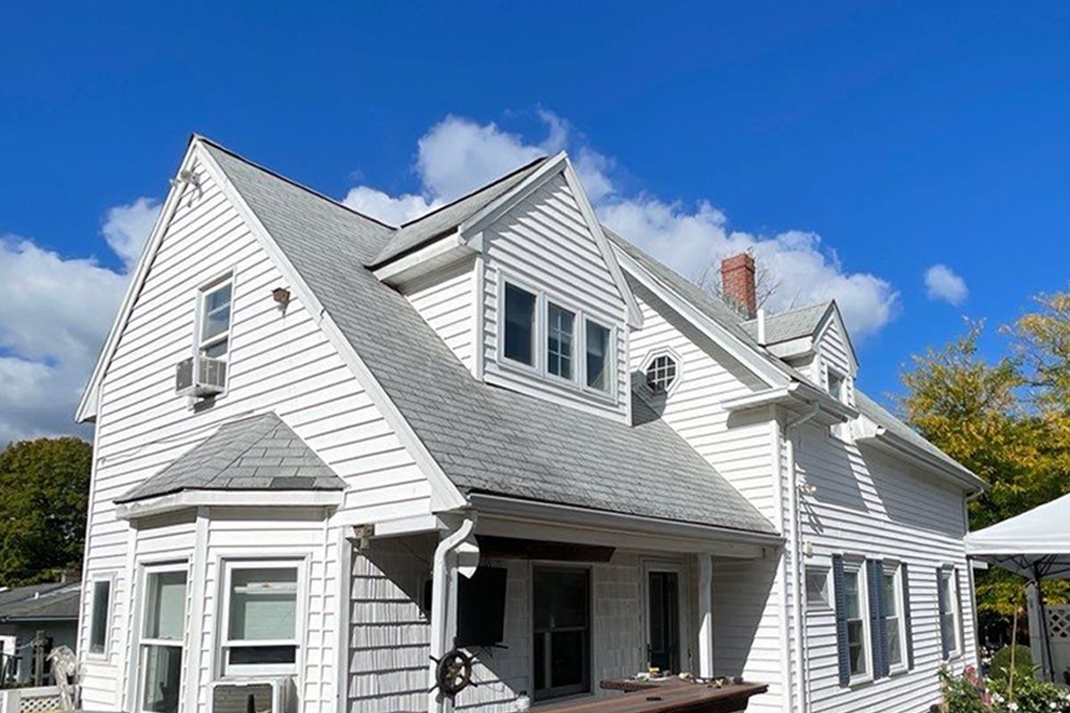 A large white house with a gray roof and a blue sky in the background.