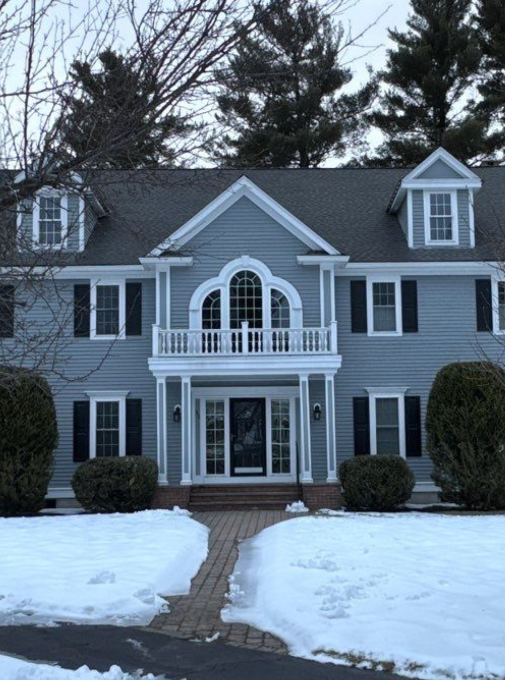 A large white house with a gray roof and a blue sky in the background.