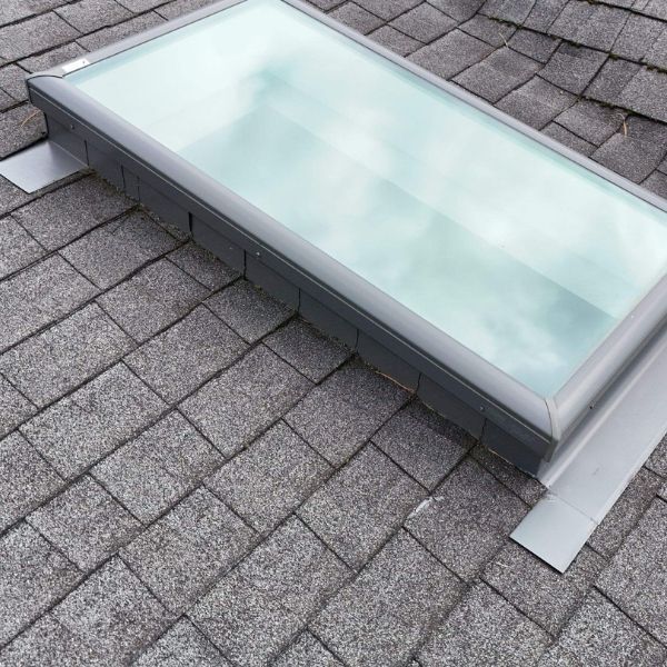 Skylight on a gray asphalt shingle roof. The glass reflects the sky.