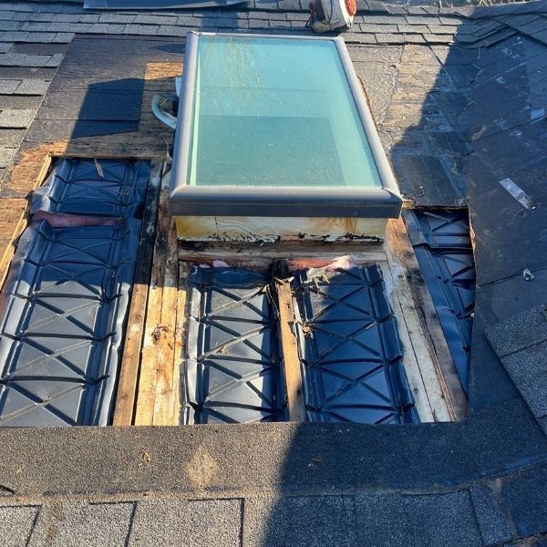 Roof with damaged shingles and a skylight, showing exposed framing.