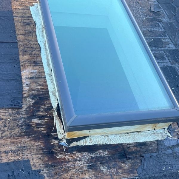 Skylight on a dark roof with visible water damage. The frame is dark, and the glass is reflective.