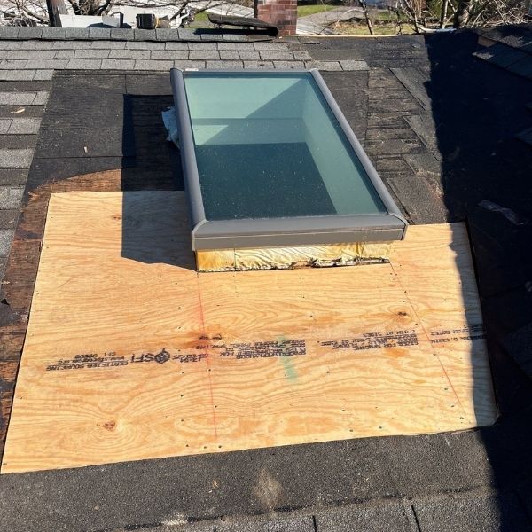 Skylight installed on a shingle roof with plywood around its base.