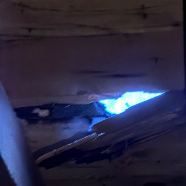 Daylight visible through damaged wood roof decking inside a Grafton, MA home.