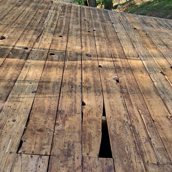 Exposed wood plank roof decking with damaged and open sections during roof replacement.