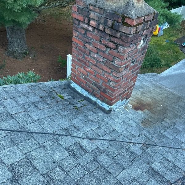 Leaning brick chimney on a gray shingled roof, outdoors.