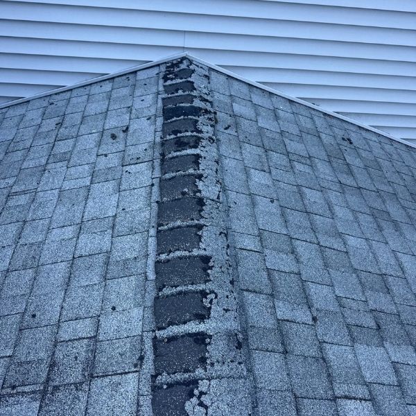 Gray asphalt shingle roof, with a ridge of dark sealant and white siding in the background.