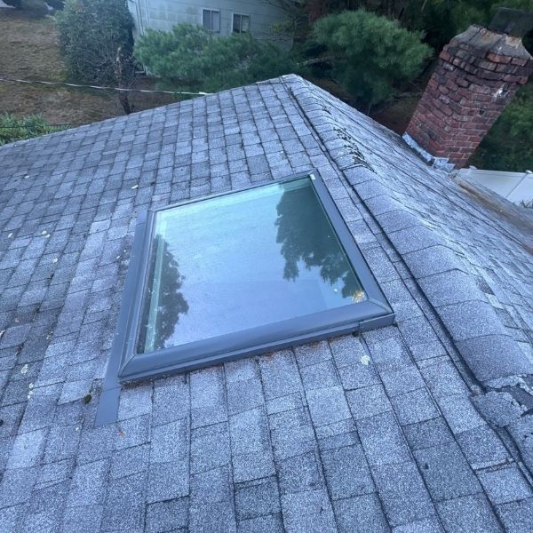 Rooftop with a skylight and brick chimney, covered in gray asphalt shingles.