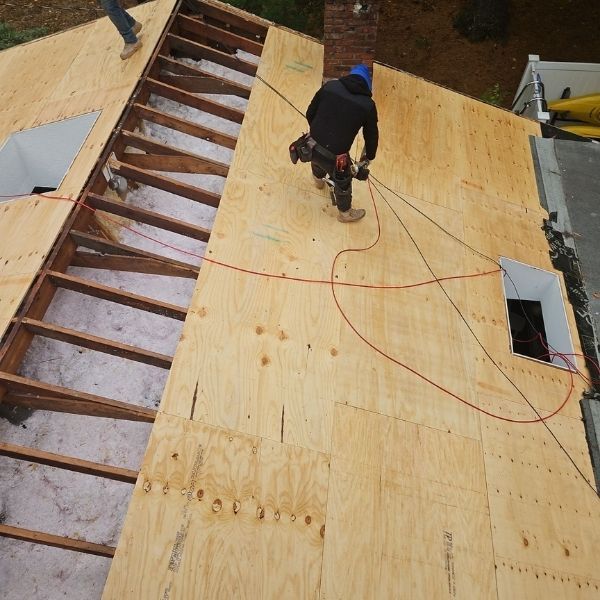 Roofer on a plywood roof installing, working, wearing safety equipment, daylight.