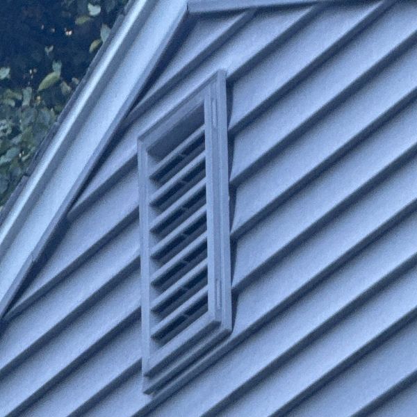 Rectangular louvered vent in gray siding on a house.