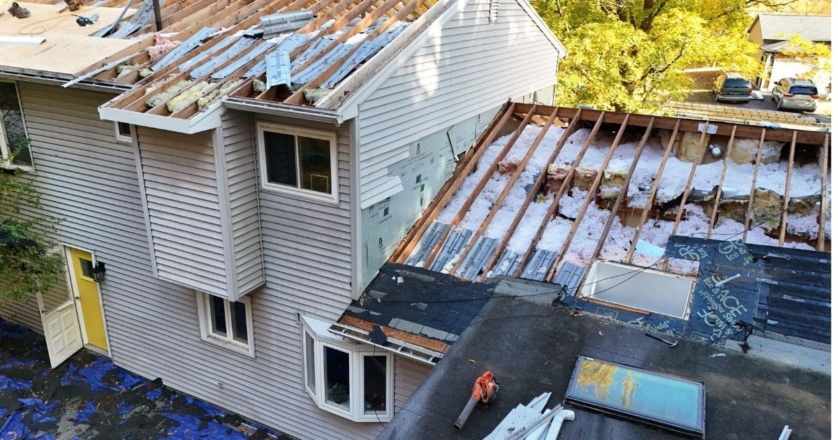 House undergoing roof and siding renovation; exposed beams, insulation, and new siding visible.