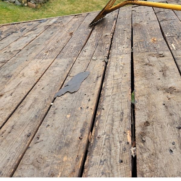 Wooden deck with a rake, weathered boards, and a piece of peeling material.