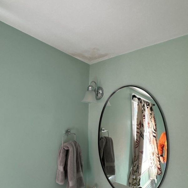 Bathroom with green walls, a circular mirror, and water damage on the ceiling.