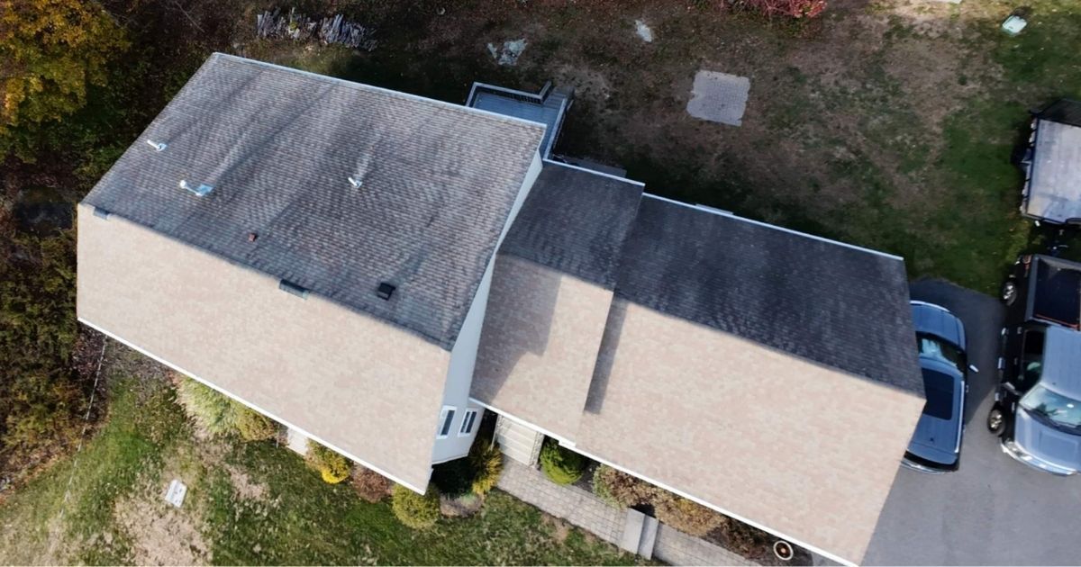 Overhead view of a house with a gray roof and tan siding. Several cars parked in the driveway.