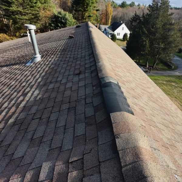Roof with weathered shingles; a vent pipe and a house are visible in the distance.