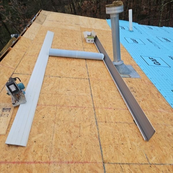 Rooftop construction: Saw, guttering, vent pipe, and roofing underlayment on plywood deck.
