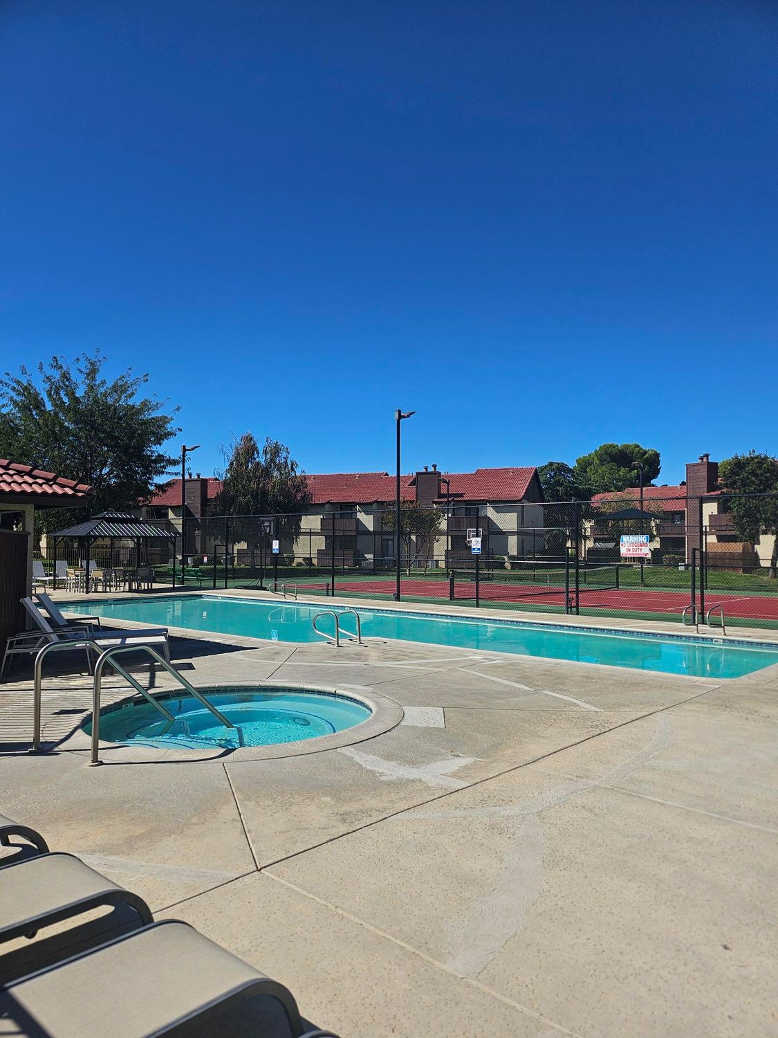 Pool area with blue sky, pool, hot tub, and apartment buildings.
