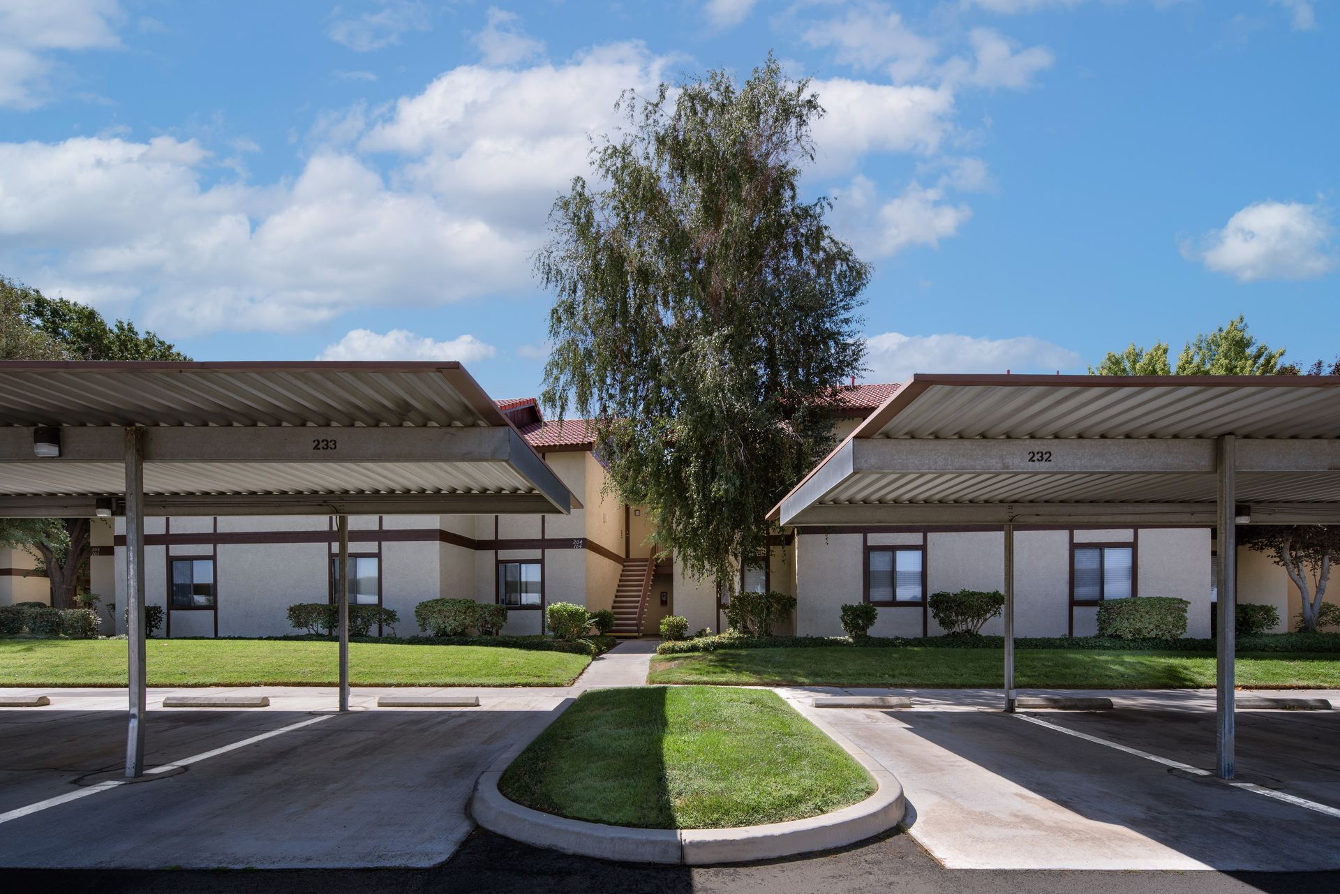 Apartment building with covered parking and grassy median on a sunny day.
