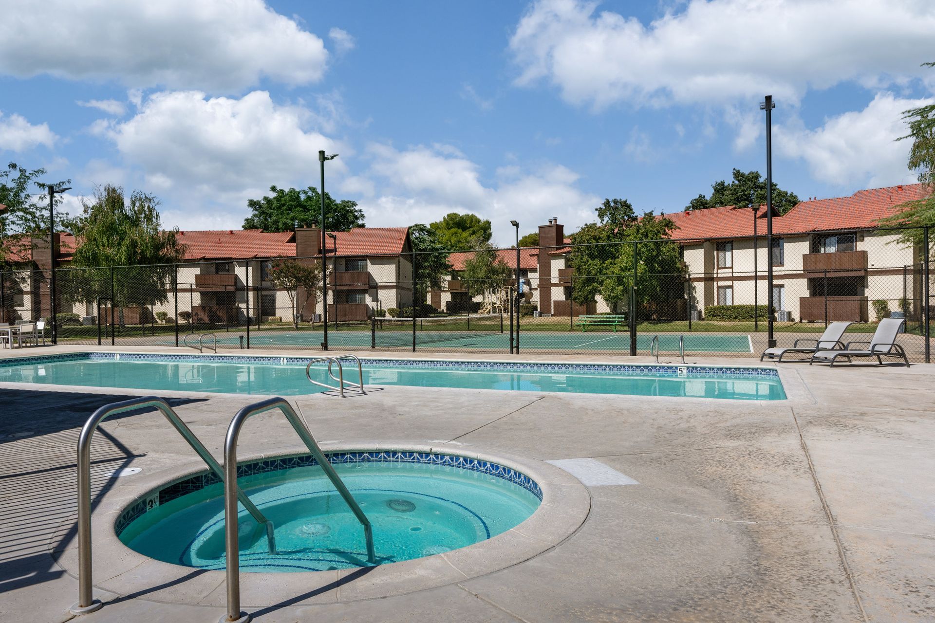 Pool and hot tub in front of two-story apartments on a sunny day.