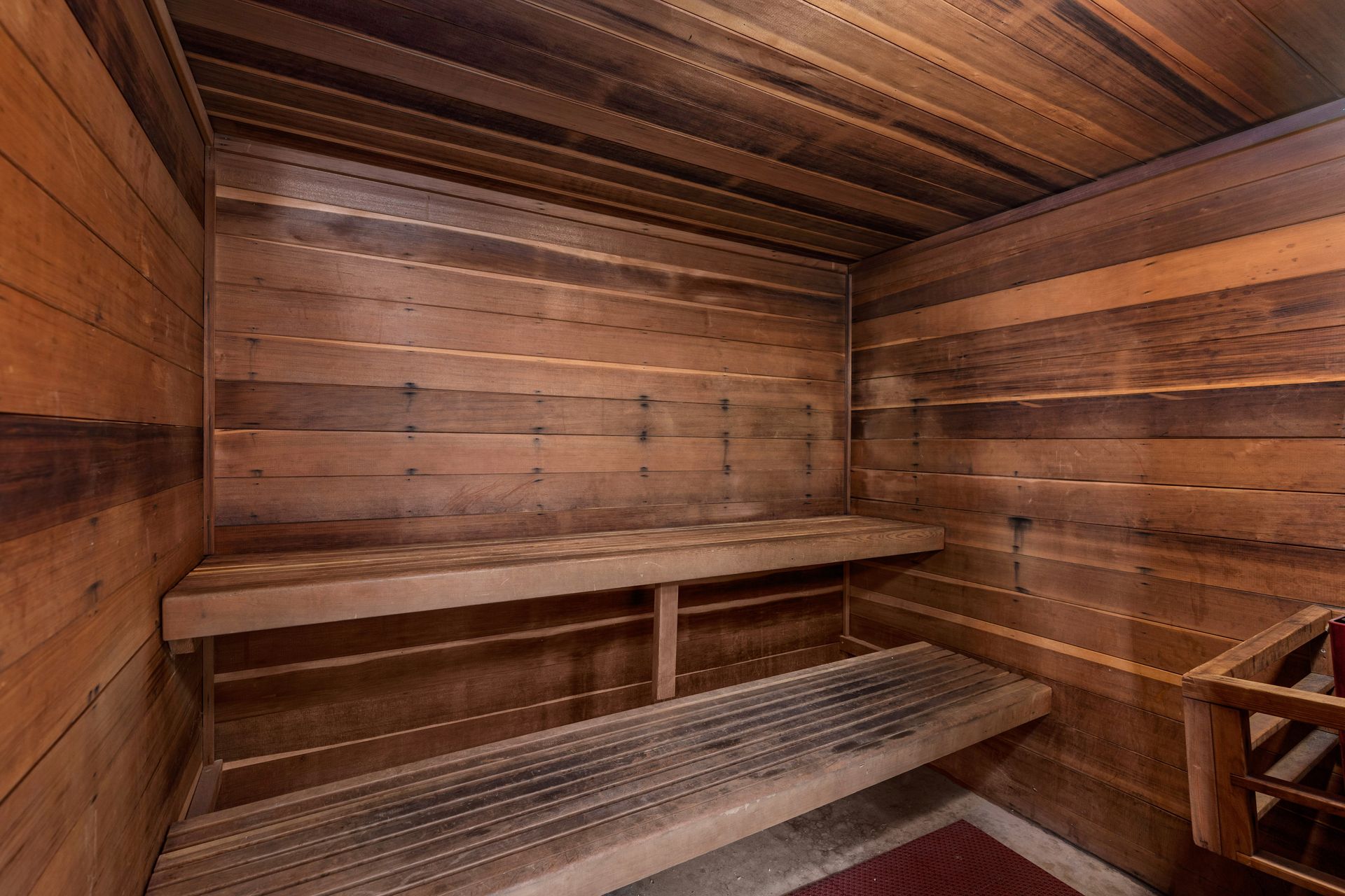 Wooden sauna interior with two-tiered benches, cedar wood panels, and a red mat on the floor.