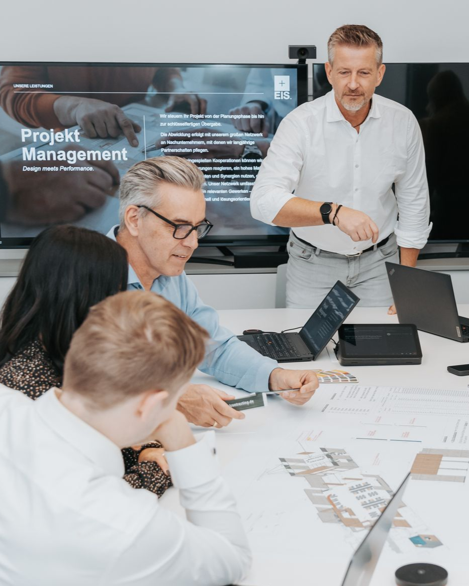 Gruppenbild vor dem EIS Aschaffenburg bei einem Teammeeting. Unser Team besteht aus Projektleitern, Bauleitern, Kalkulator, Einkäufer, Architekt, Innenarchitekt und vieles mehr. Wir stellen ein! Offene Jobs im Bauunternehmen