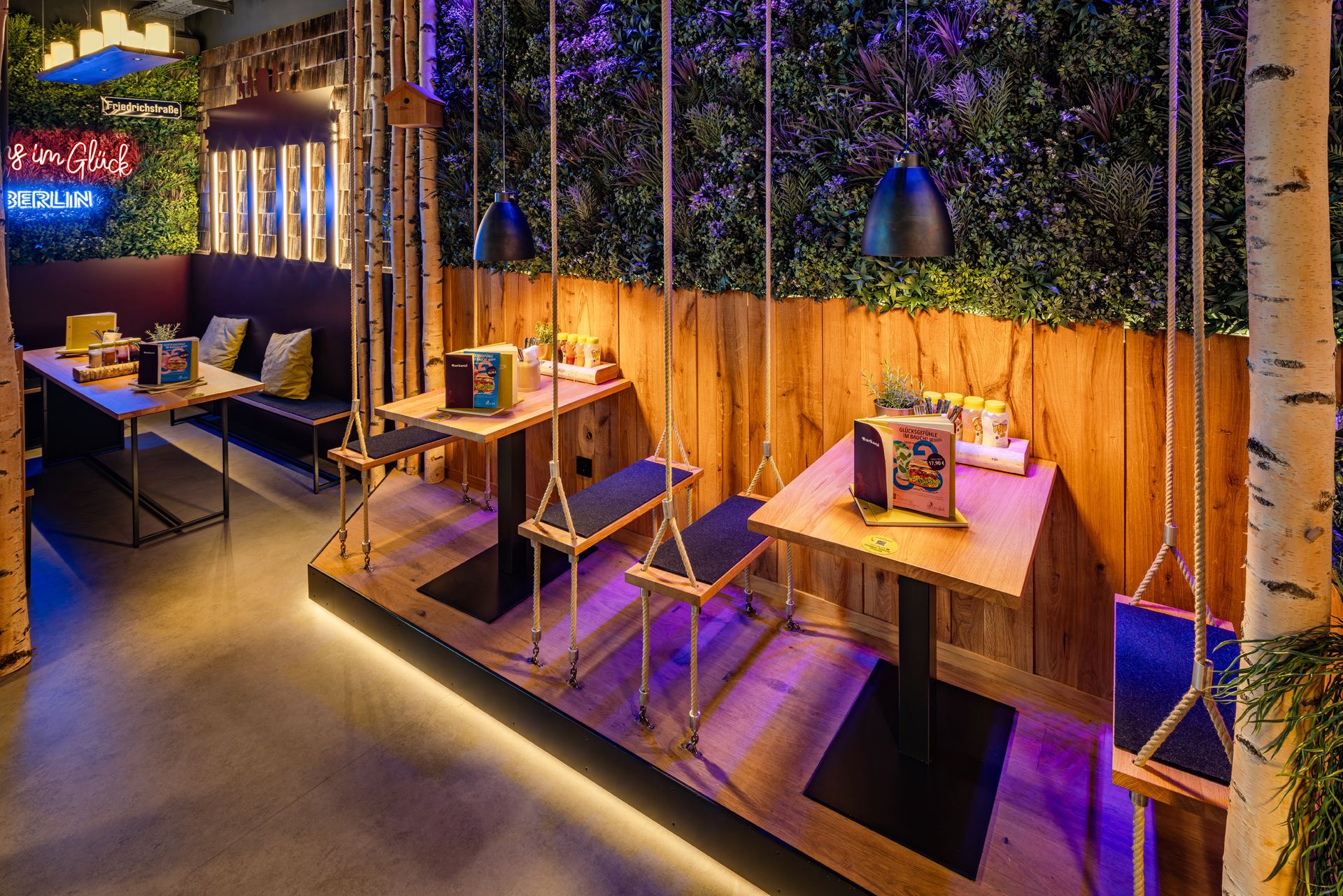 Innenraum von "Hans im Glück" in Berlin. Gemütliche Bar mit Birkenstämmen, vielen Flaschen, Pflanzen & warmer Beleuchtung.