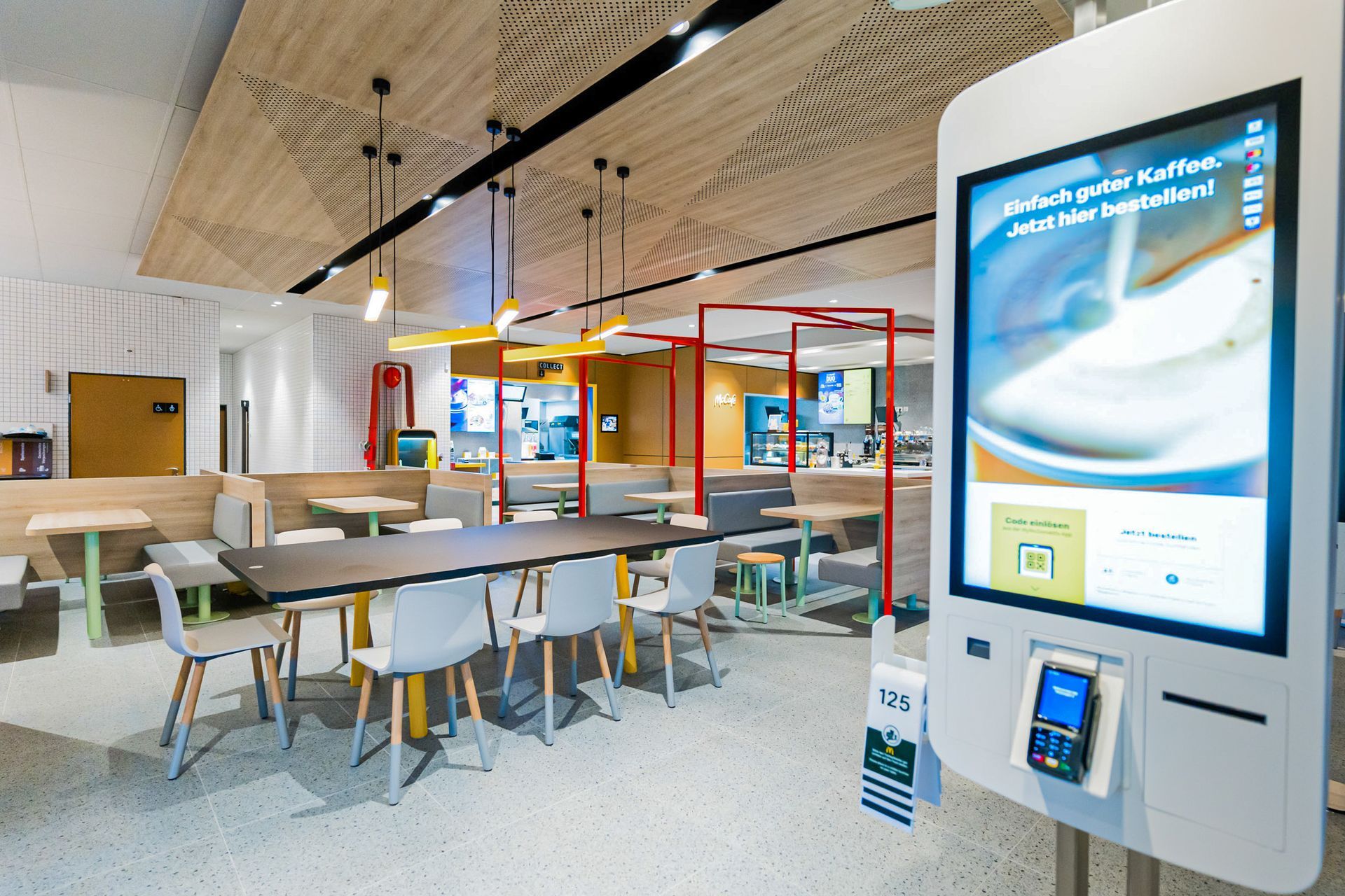 McDonald's Human Comfort Kaiserslautern - Raumansicht eines modernen Fast-Food-Restaurants mit schwarzem maßgefertigtem Holztisch, und weiße Stühle und Bestellbildschirmen - Referenzprojekt Generalunternehmer Innenausbau