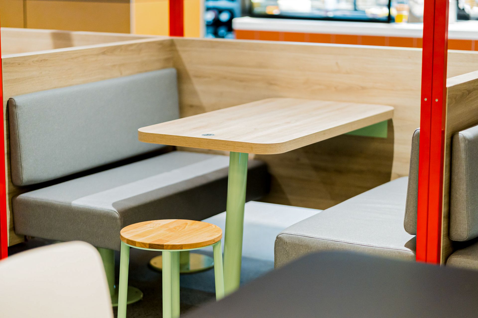 McDonald's Human Comfort Kaiserslautern - Nahansicht maßgeschneiderter Sitzmöbel und Tisch. Graue Sitzbank und integrierter Holztisch aus der Schreinerei - Referenzprojekt Generalunternehmer Innenausbau