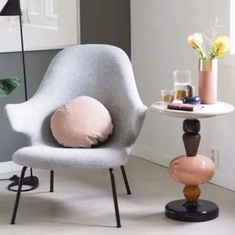 Un scaun cu o pernă pe el stă lângă o măsuță cu o vază cu flori pe el