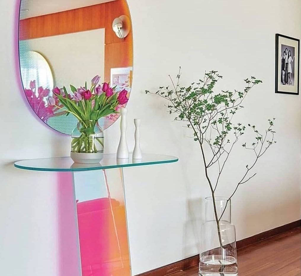 O vază cu flori stă pe o masă de sticlă lângă o oglindă