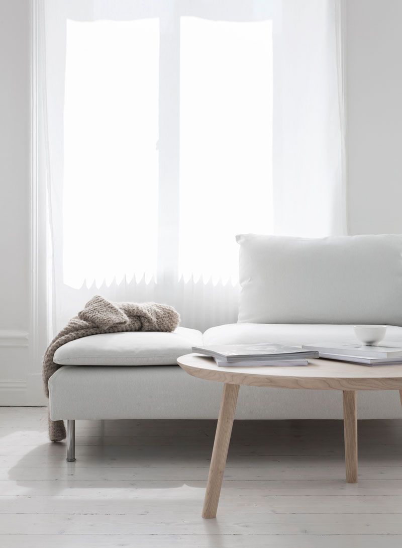 O canapea albă stă lângă o măsuță de cafea din lemn într-o cameră de zi.