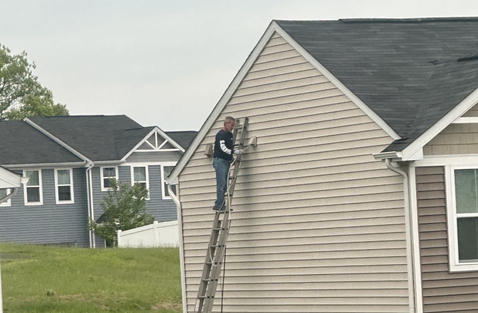 Person on ladder working on siding of a house.