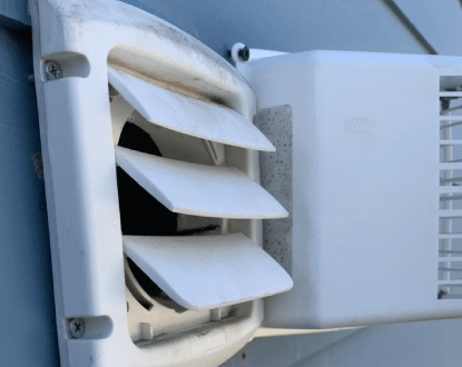 White dryer vent with three angled flaps on a blue wall.