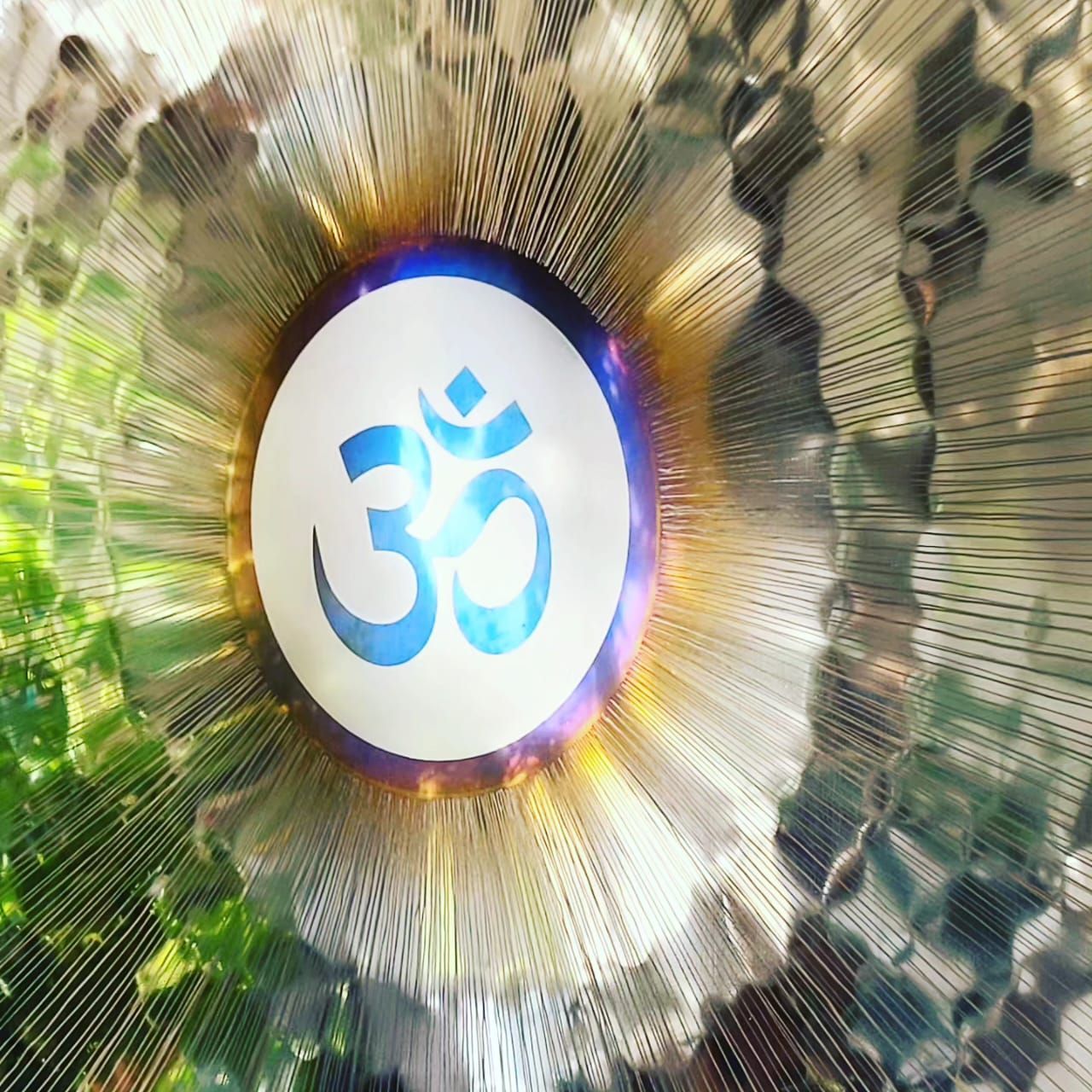 Un gong de metal brillante con el símbolo Om, rodeado de un efecto de explosión de luz, en un entorno natural al aire libre.
