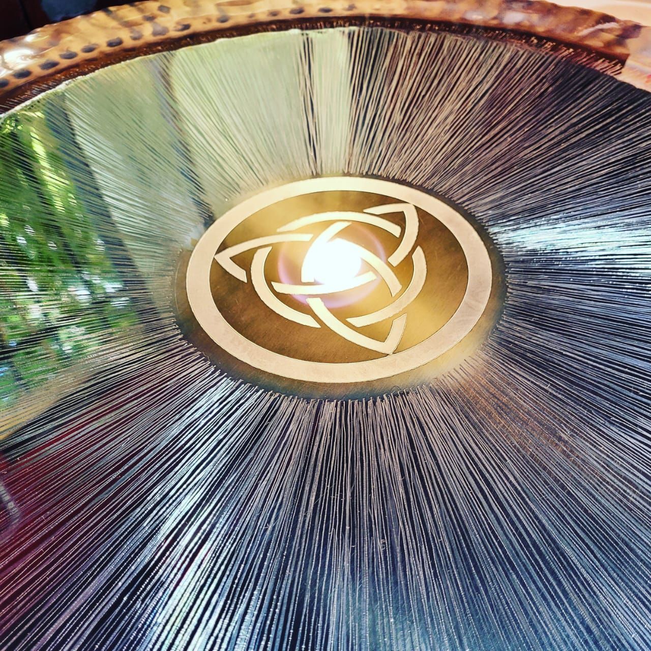 Gong metálico con emblema central dorado y ranuras radiales.