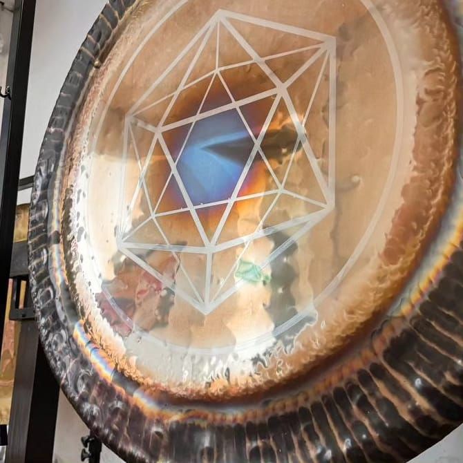 Primer plano de un gran gong circular con un símbolo geométrico grabado en el centro. 