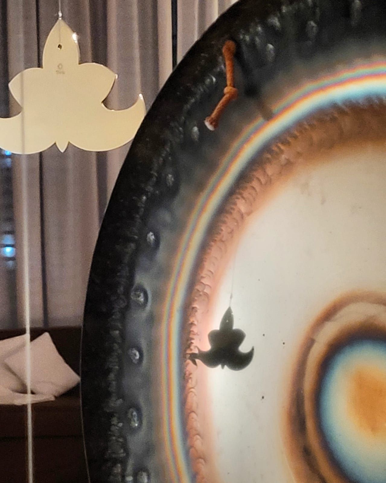 Primer plano de un gran gong circular con los colores del arcoíris reflectantes. Cerca cuelgan dos adornos con forma de flor.