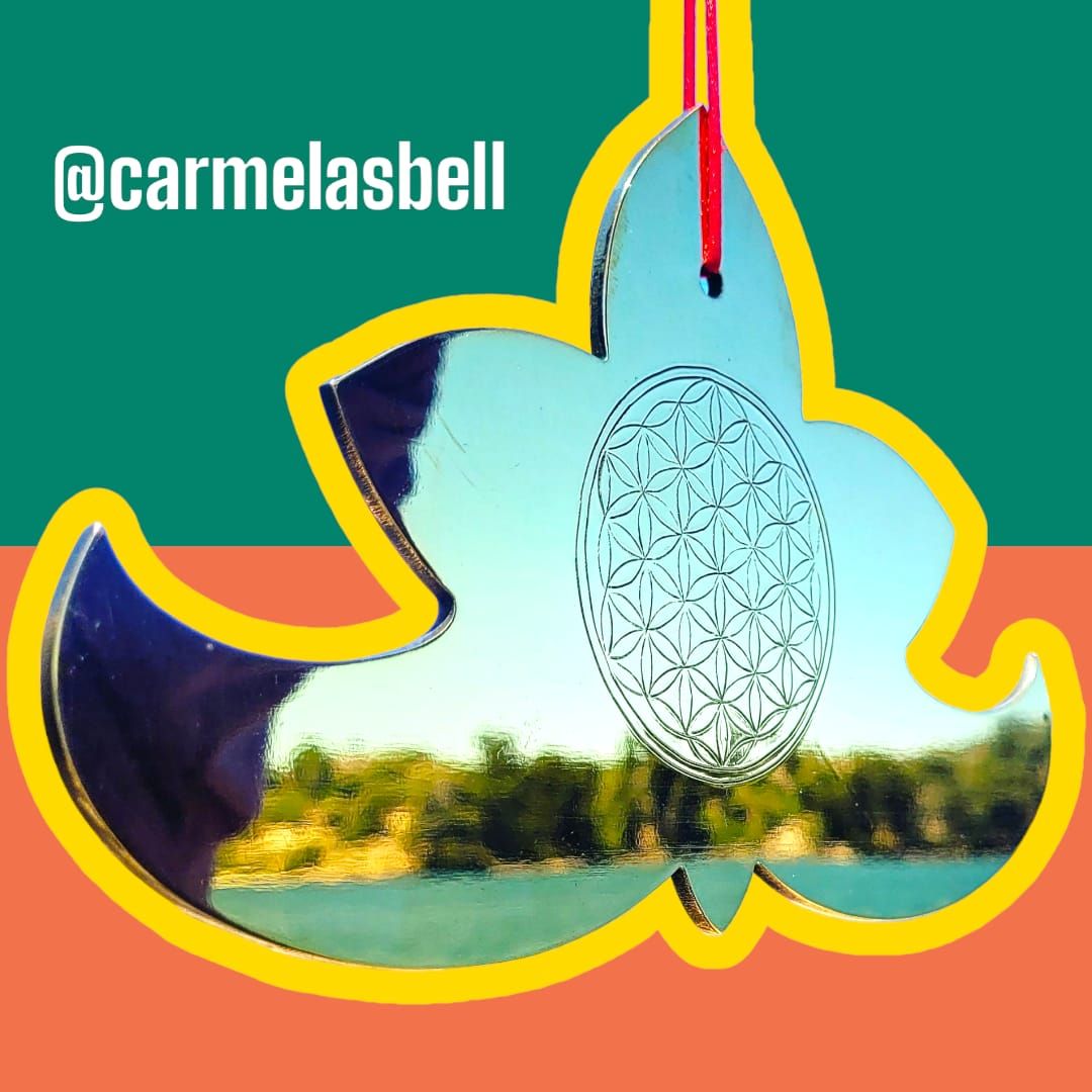 Un adorno de espejo en forma de hoja con un diseño floral que refleja un lago y árboles.