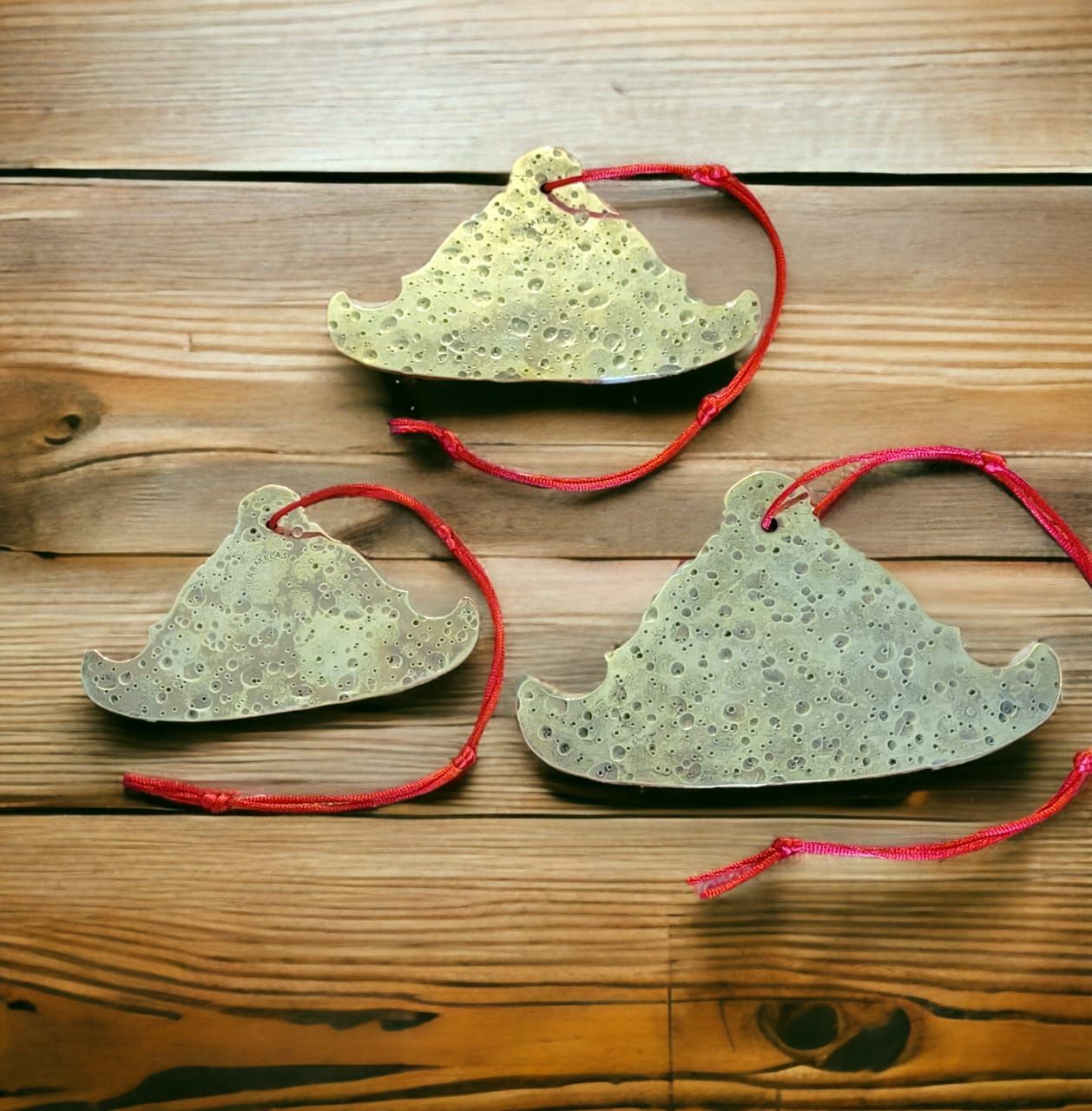 Tres adornos decorativos en forma de montaña, de color dorado, con hilo rojo sobre una superficie de madera.